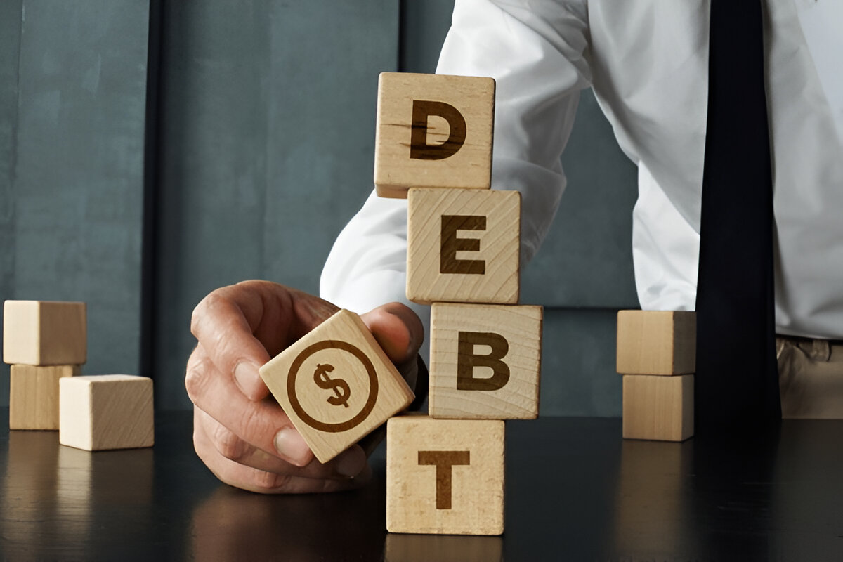 Business person in white shirt arranging wooden blocks spelling 'DEBT' with dollar sign symbol block, demonstrating financial planning concept